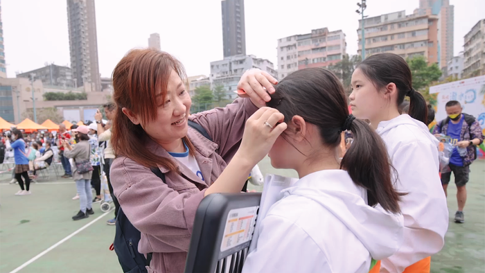 「家長義工」吳崇熙媽媽在樂團表演前，細心為團員整理頭髮。